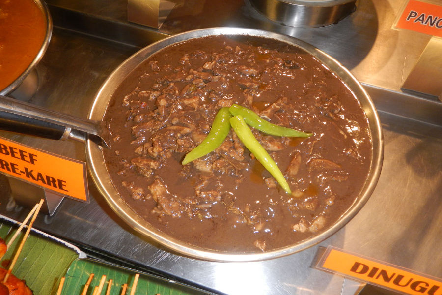 A dark, savory bowl of Dinuguan (pork blood stew) served with puto (rice cake), a popular Philippine exotic foods delicacy.