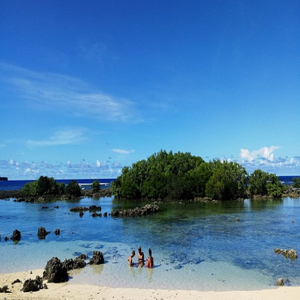 A tranquil view of Secret Beach (Guiwan Beach) in Siargao, Philippines, showing clear turquoise water, a sandy shoreline fringed with islets and gentle waves. Awesome Philippine travel destination.